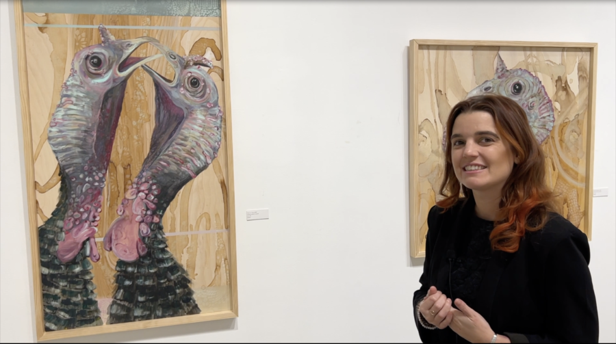Artist Caitlin Gill stands in front of two pieces from her "Fowl Play" exhibit.
